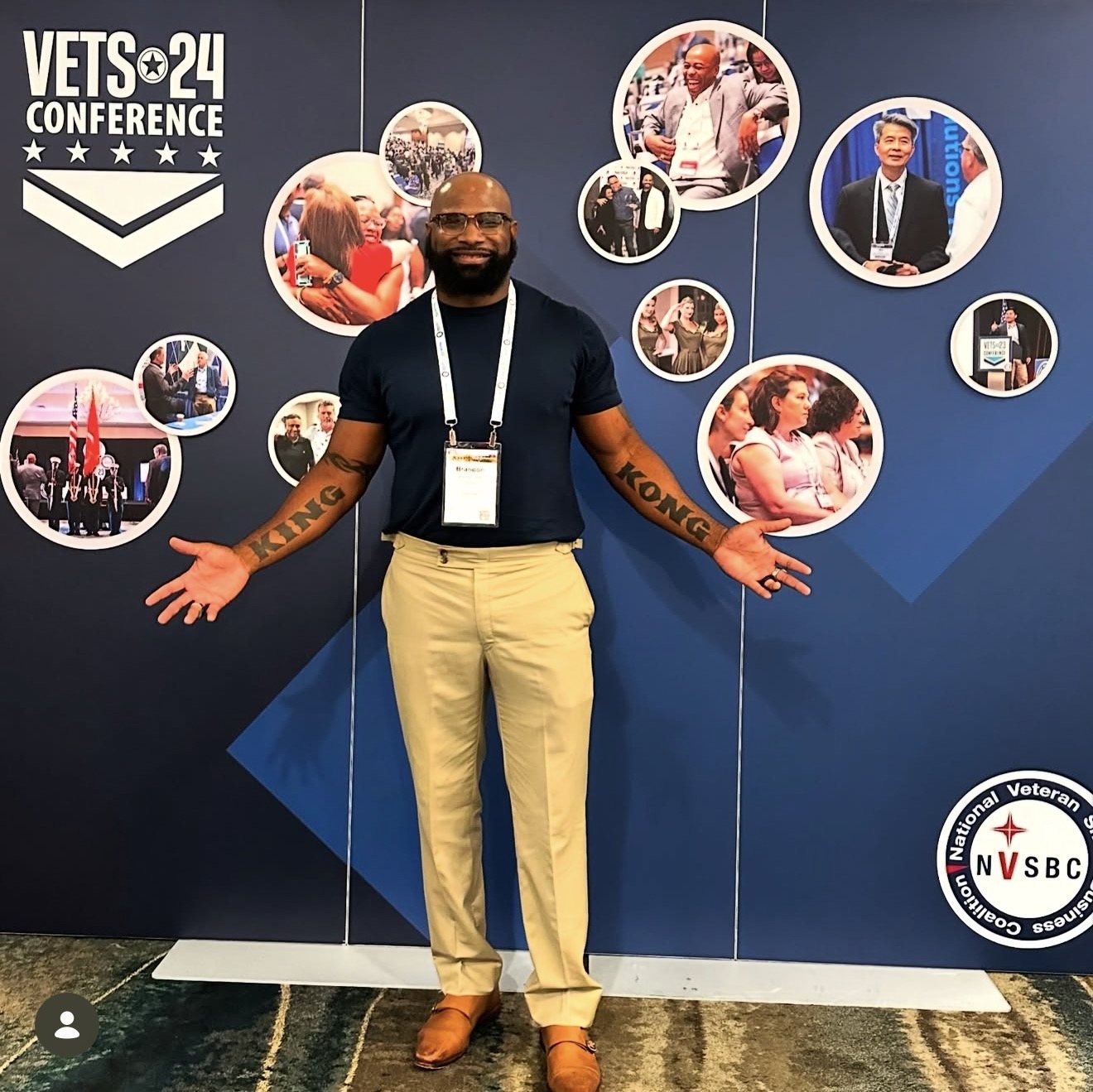 A Love4Vets team member standing with arms open in front of a VETS 24 Conference backdrop.