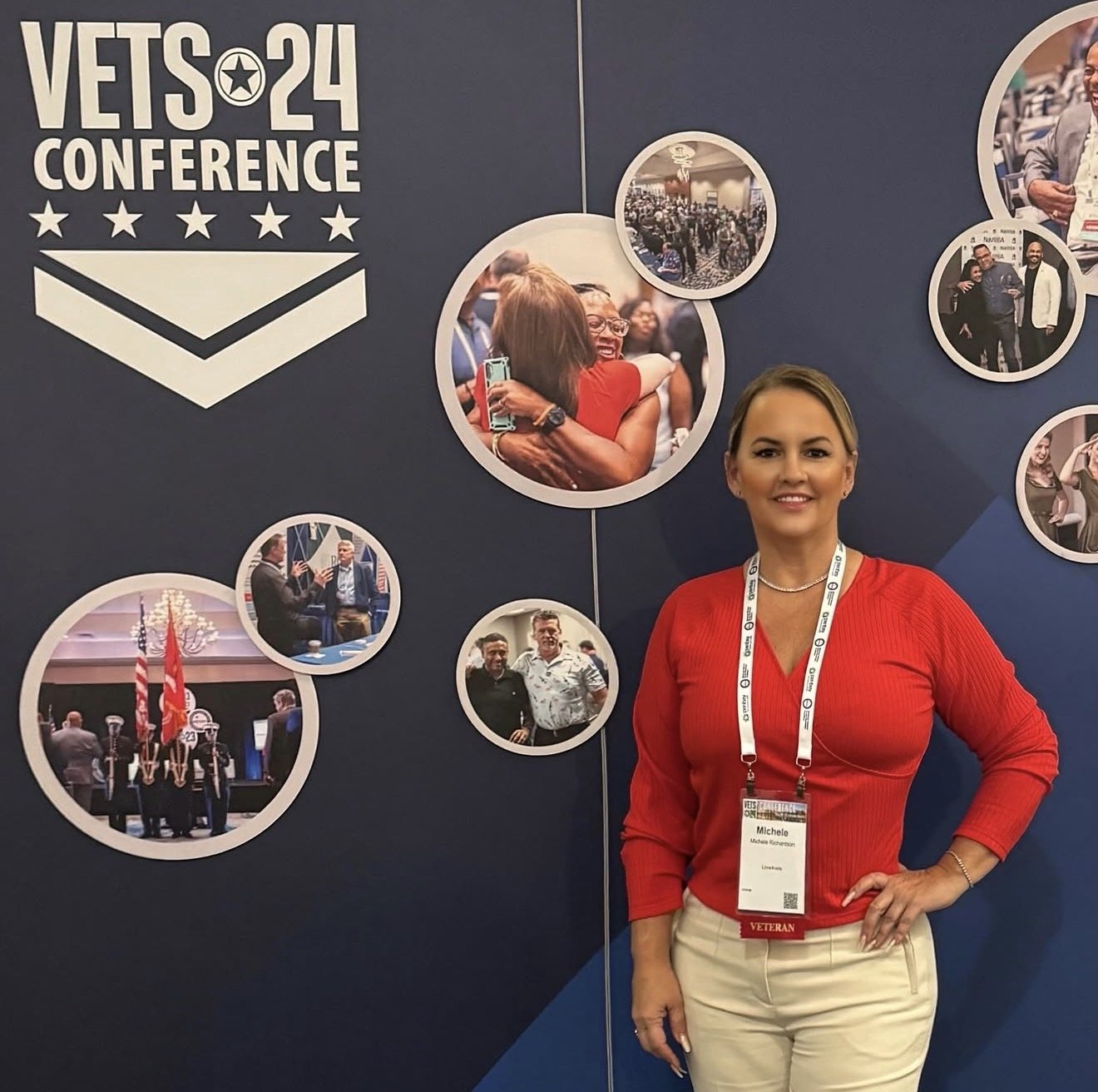 A Love4Vets team member standing in front of a VETS 24 Conference display wall.