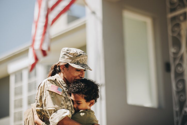 A service member holding her young child close outside their home.